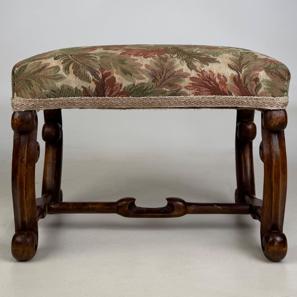 An Edwardian rectangular low stool featuring a carved dark walnut frame with scroll legs, an H-stretcher, and botanical tapestry upholstery. View V