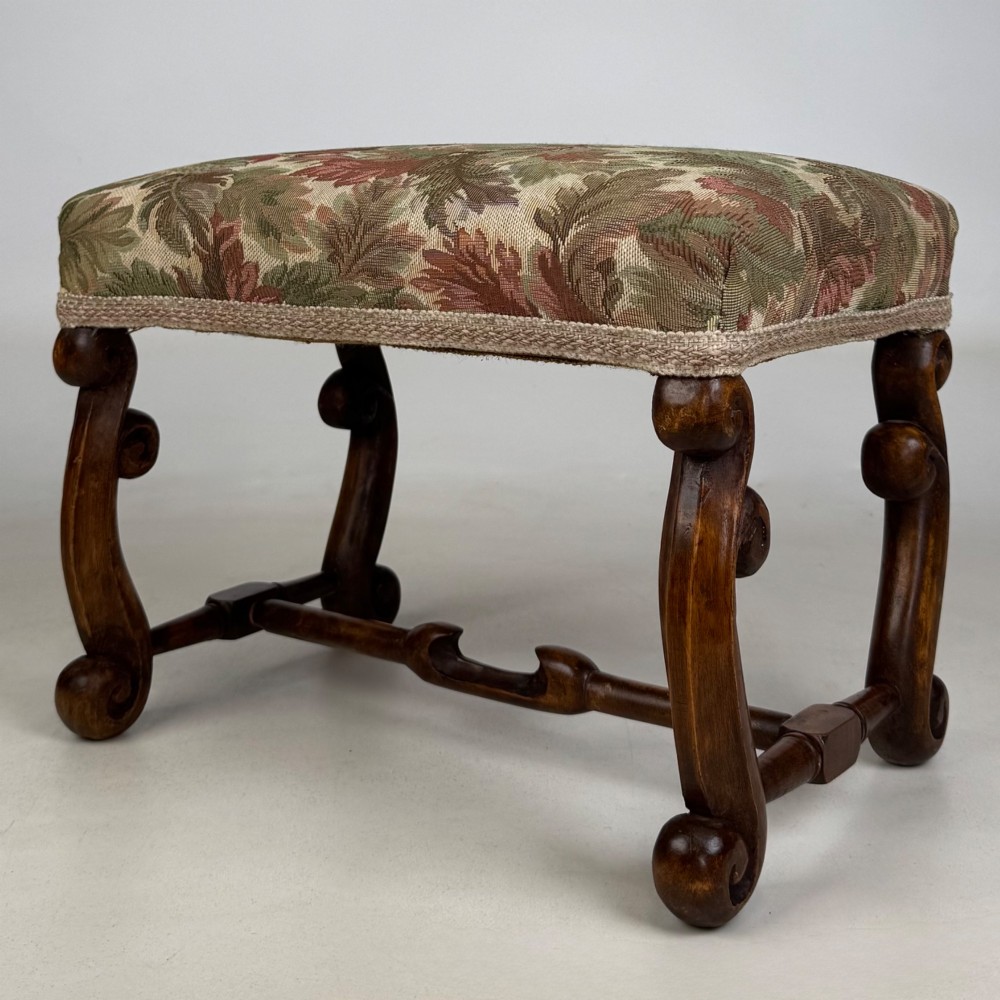 An Edwardian rectangular low stool featuring a carved dark walnut frame with scroll legs, an H-stretcher, and botanical tapestry upholstery. View VI