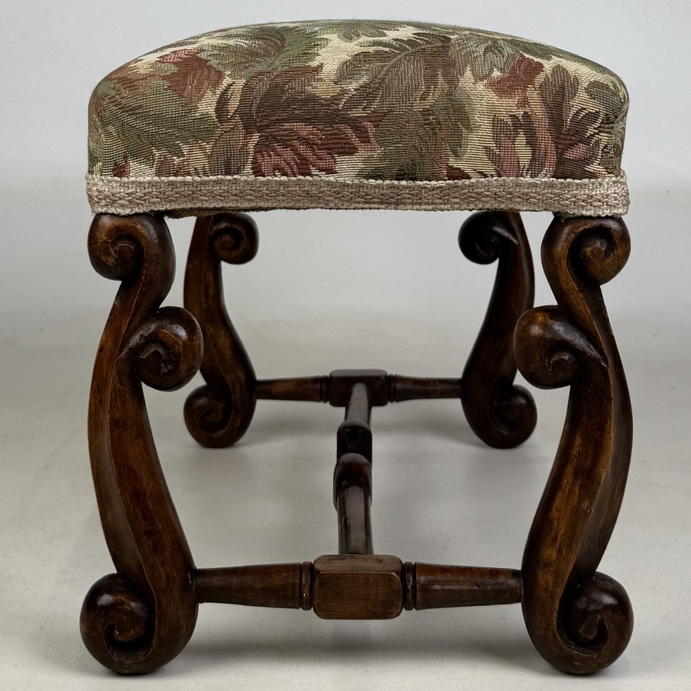 An Edwardian rectangular low stool featuring a carved dark walnut frame with scroll legs, an H-stretcher, and botanical tapestry upholstery. View VII
