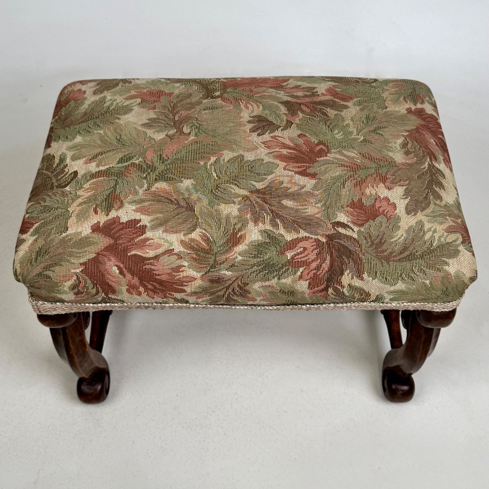 An Edwardian rectangular low stool featuring a carved dark walnut frame with scroll legs, an H-stretcher, and botanical tapestry upholstery. View IX