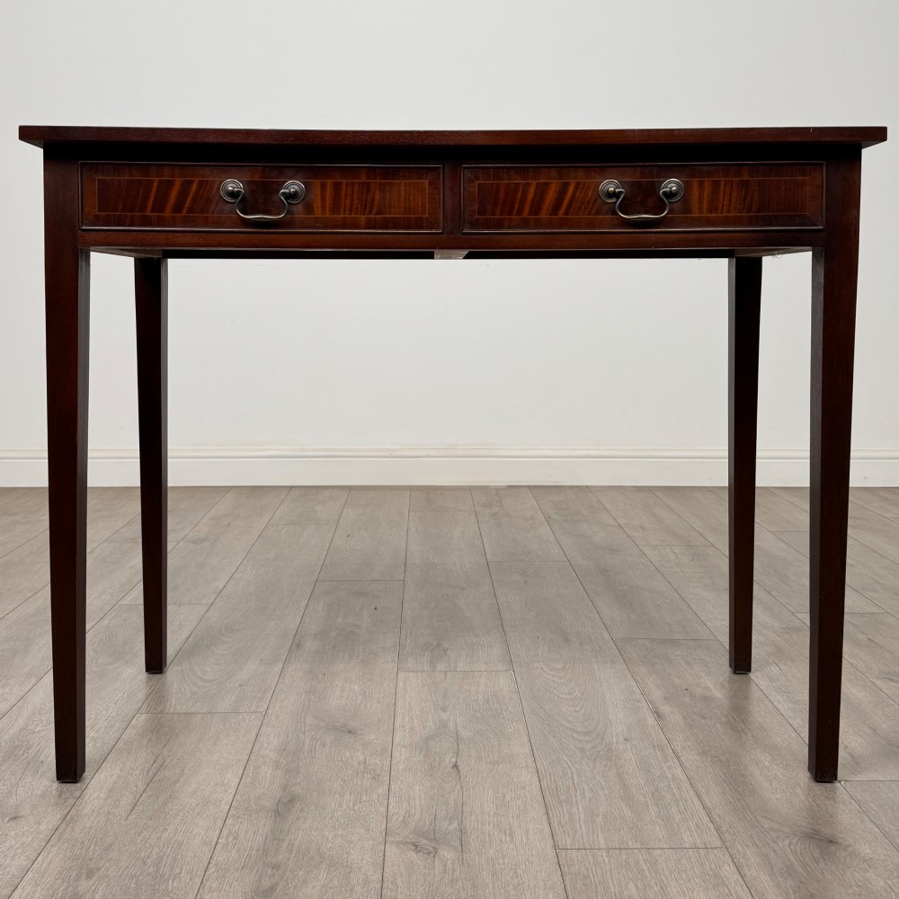 A dark mahogany writing table featuring two frieze drawers with brass swan-neck handles and tapered square legs.
