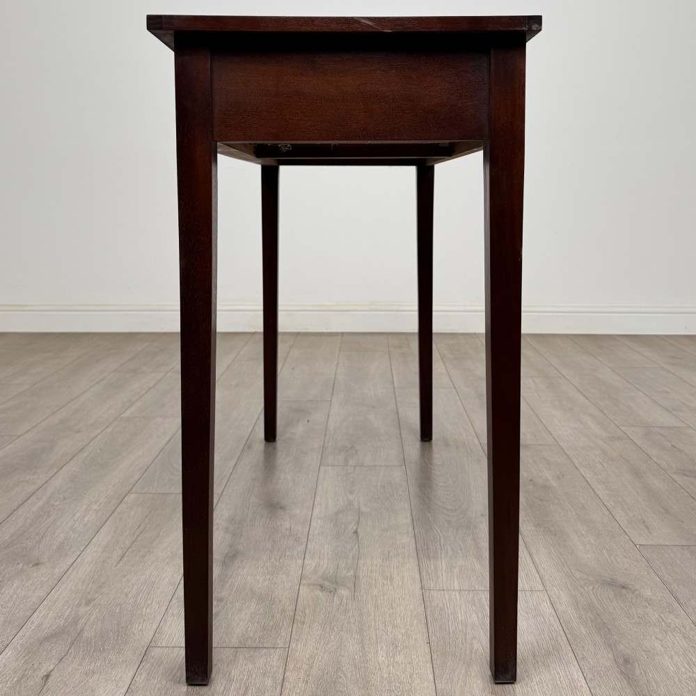 A dark mahogany writing table featuring two frieze drawers with brass swan-neck handles and tapered square legs. View III