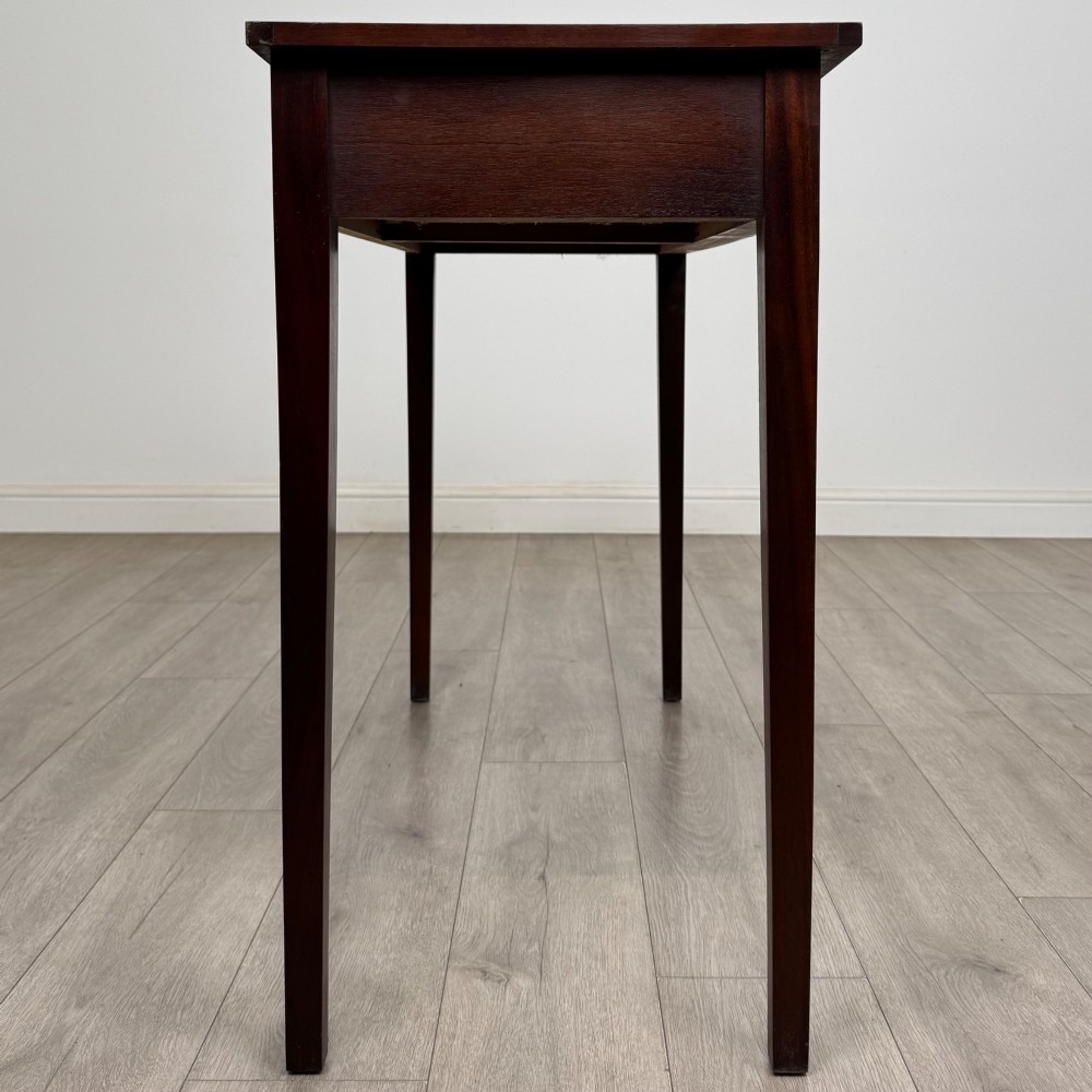 A dark mahogany writing table featuring two frieze drawers with brass swan-neck handles and tapered square legs. View VII