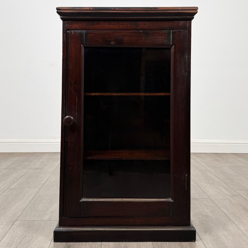 A dark brown stained Edwardian pine glazed cabinet featuring a single glass door with a turned wooden handle and internal shelves.