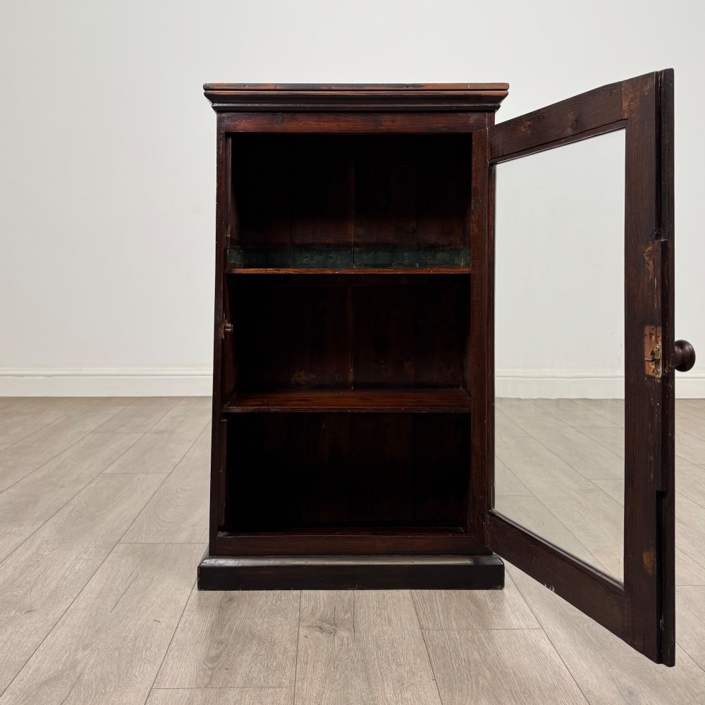 A dark brown stained Edwardian pine glazed cabinet featuring a single glass door with a turned wooden handle and internal shelves. View II