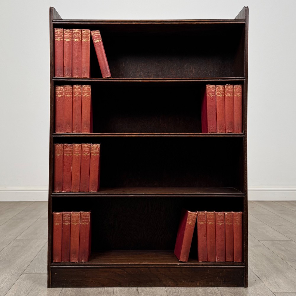 An antique dark oak open bookcase featuring four horizontal shelves with raised side galleries and a solid plinth base.