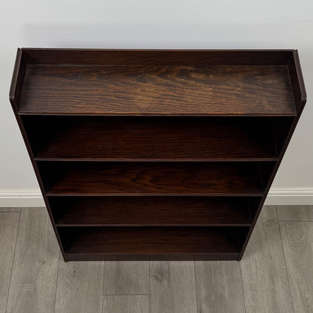 An antique dark oak open bookcase featuring four horizontal shelves with raised side galleries and a solid plinth base. View X