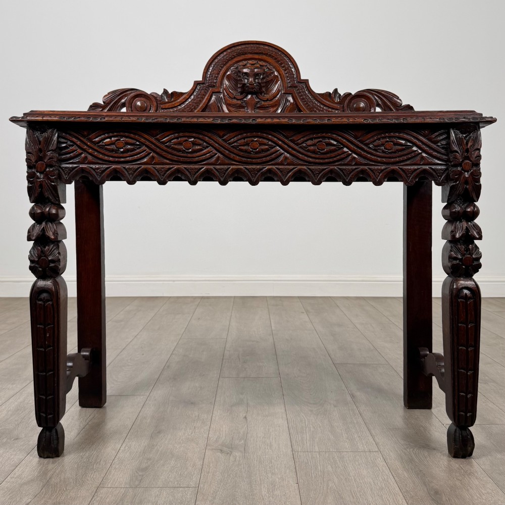 A dark brown 19th-century carved oak side table featuring an ornate splashback with a lion mask carving and intricately carved legs.