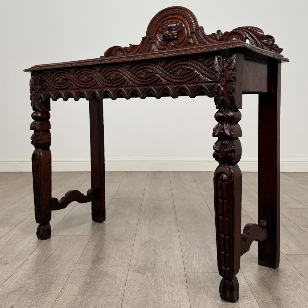 A dark brown 19th-century carved oak side table featuring an ornate splashback with a lion mask carving and intricately carved legs. View II