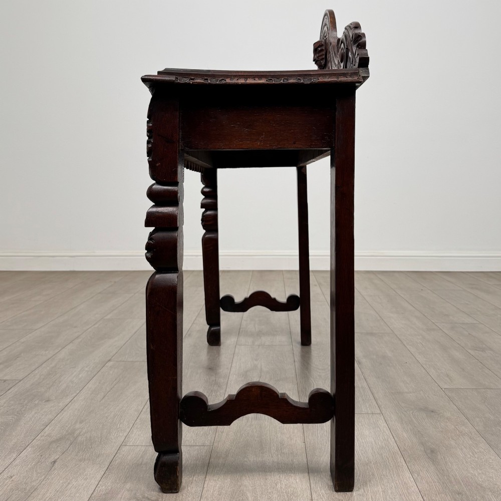 A dark brown 19th-century carved oak side table featuring an ornate splashback with a lion mask carving and intricately carved legs. View III