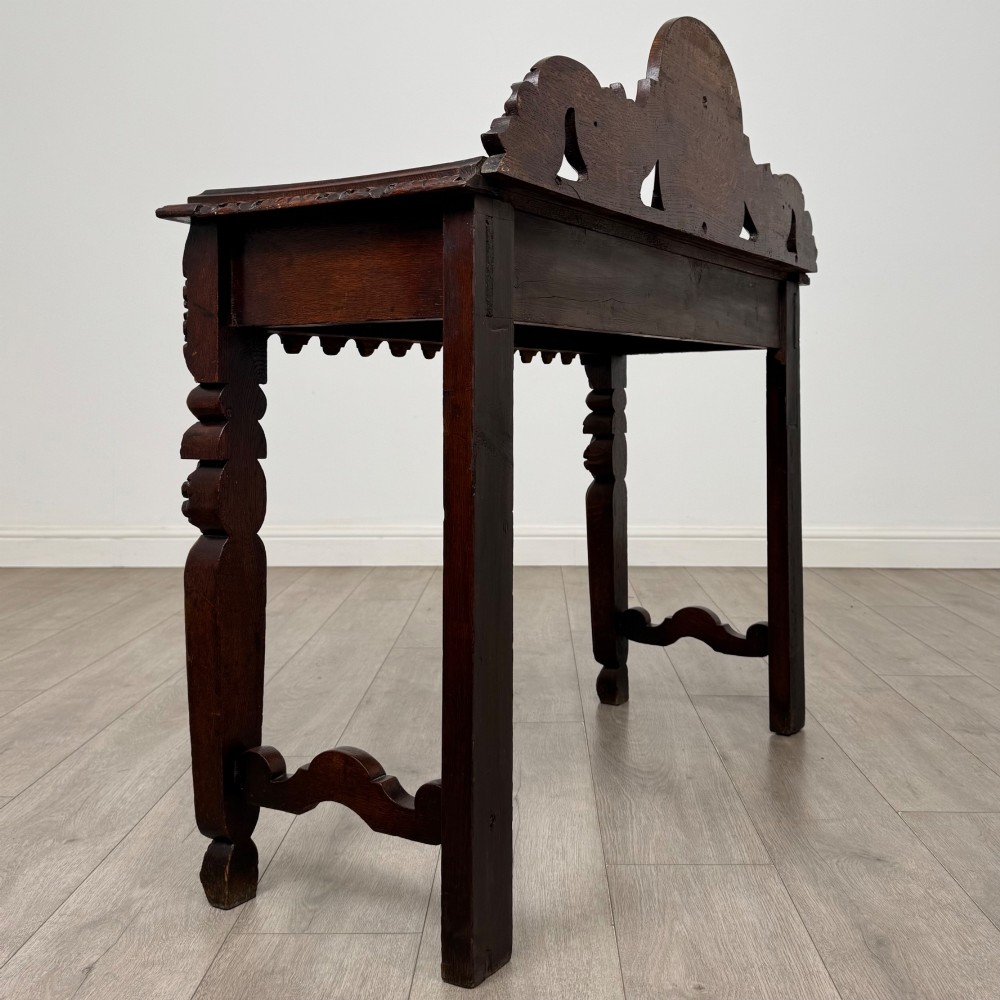 A dark brown 19th-century carved oak side table featuring an ornate splashback with a lion mask carving and intricately carved legs. View IV