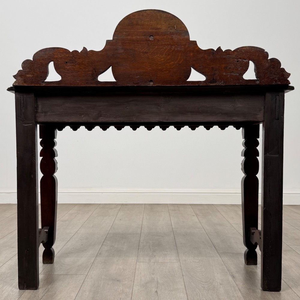 A dark brown 19th-century carved oak side table featuring an ornate splashback with a lion mask carving and intricately carved legs. View V