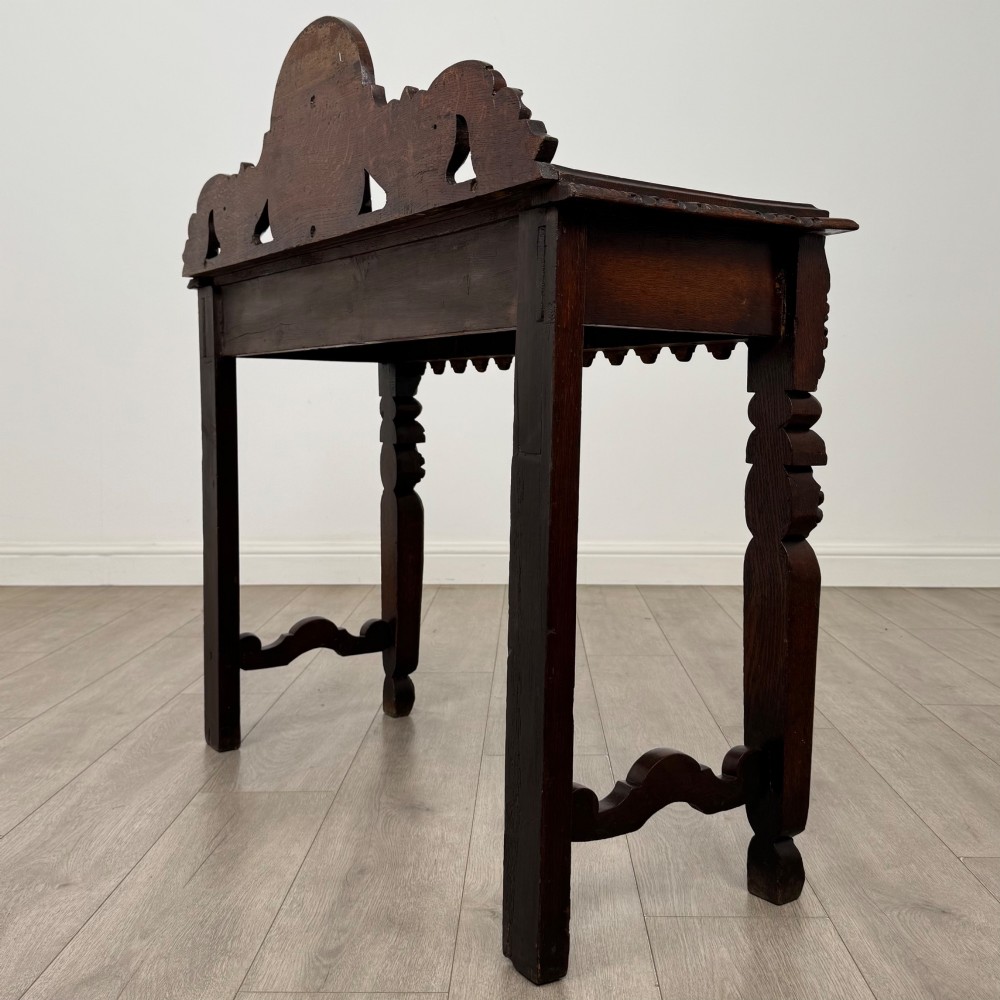 A dark brown 19th-century carved oak side table featuring an ornate splashback with a lion mask carving and intricately carved legs. View VI