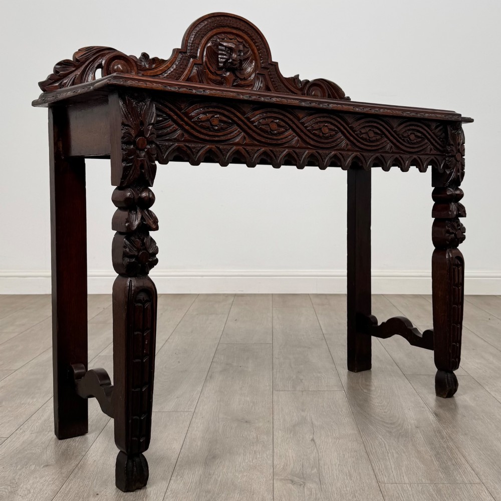 A dark brown 19th-century carved oak side table featuring an ornate splashback with a lion mask carving and intricately carved legs. View VIII