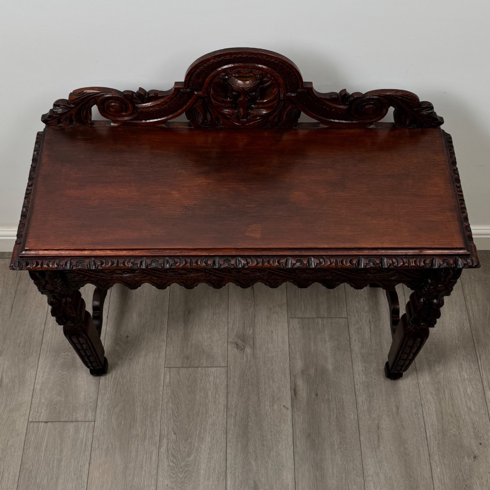 A dark brown 19th-century carved oak side table featuring an ornate splashback with a lion mask carving and intricately carved legs. View IX
