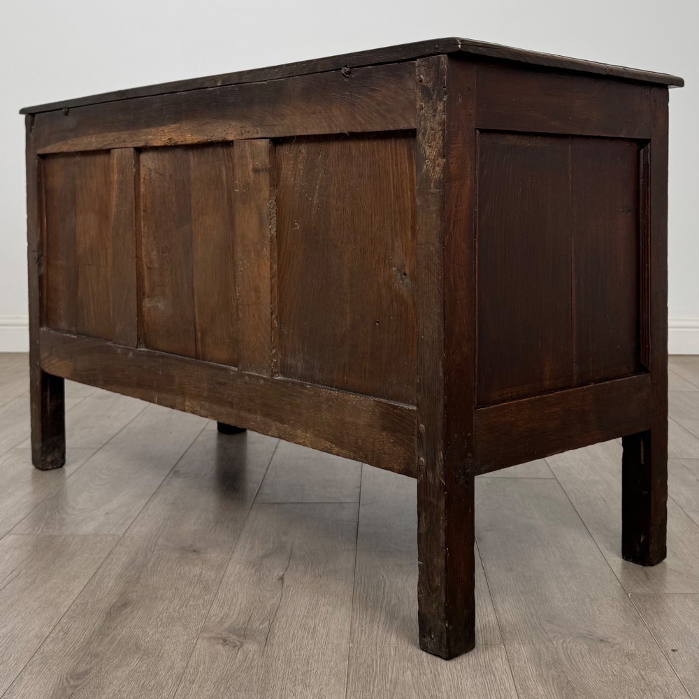 An 18th-century dark oak coffer featuring three sunken front panels, raised stiles, a hinged lid, and a central brass keyhole escutcheon. View VI