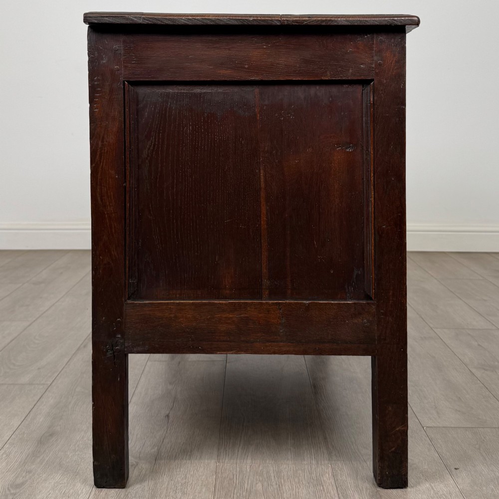 An 18th-century dark oak coffer featuring three sunken front panels, raised stiles, a hinged lid, and a central brass keyhole escutcheon. View VII