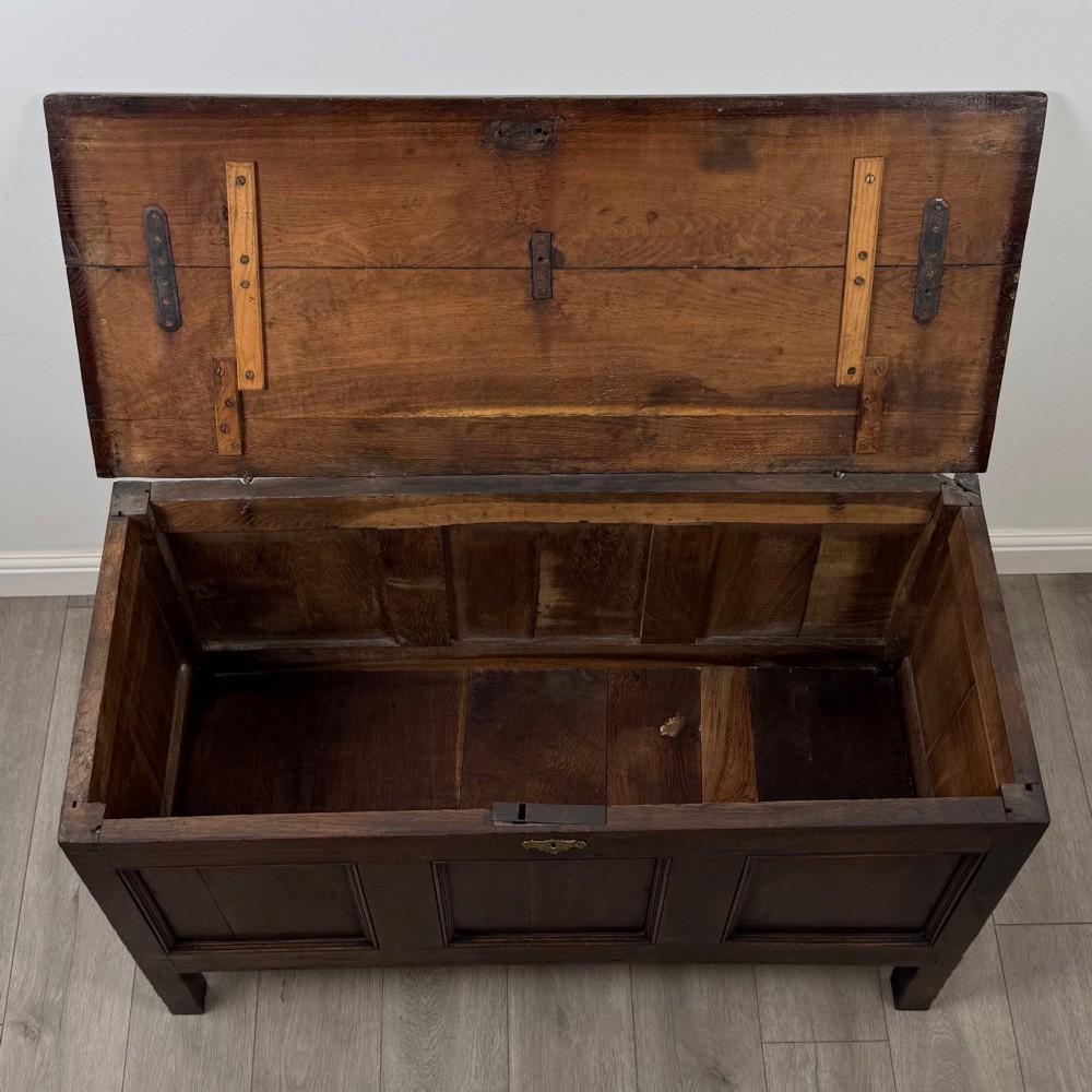 An 18th-century dark oak coffer featuring three sunken front panels, raised stiles, a hinged lid, and a central brass keyhole escutcheon. View X