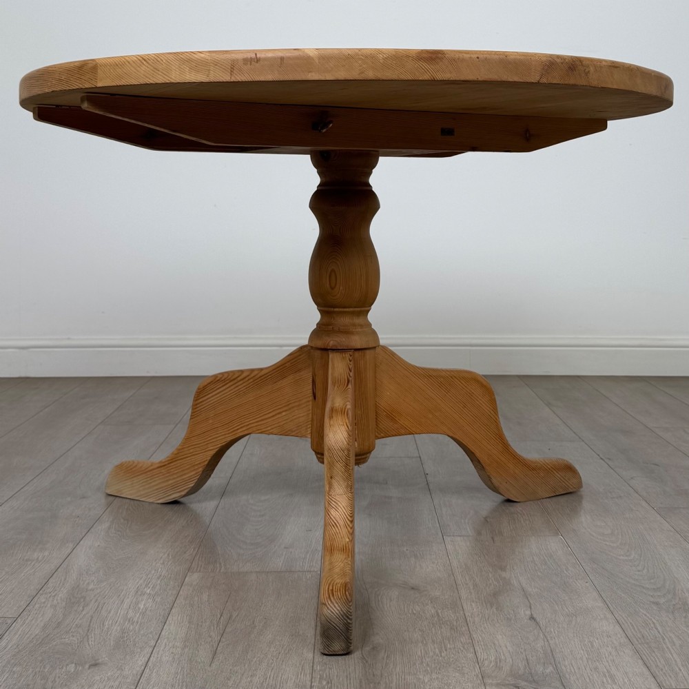 A 19th-century circular pine tilt-top breakfast table with a turned central pedestal column and splayed four-leg base.