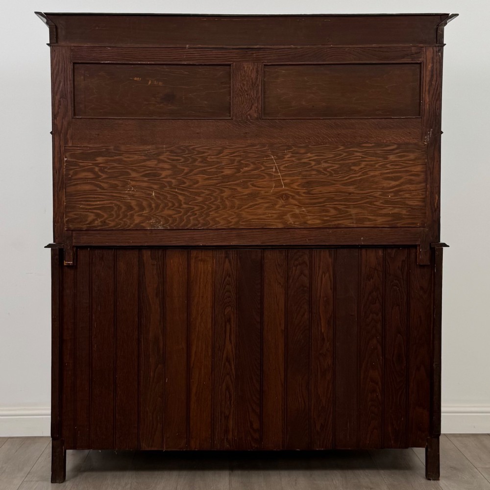 An early twentieth-century Arts and Crafts oak sideboard featuring carved floral door panels, two drawers, a mirrored backsplash, and an upper glazed cabinet. View VI