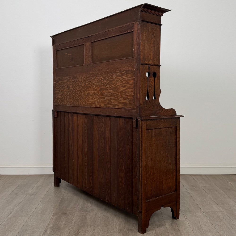 An early twentieth-century Arts and Crafts oak sideboard featuring carved floral door panels, two drawers, a mirrored backsplash, and an upper glazed cabinet. View VIII