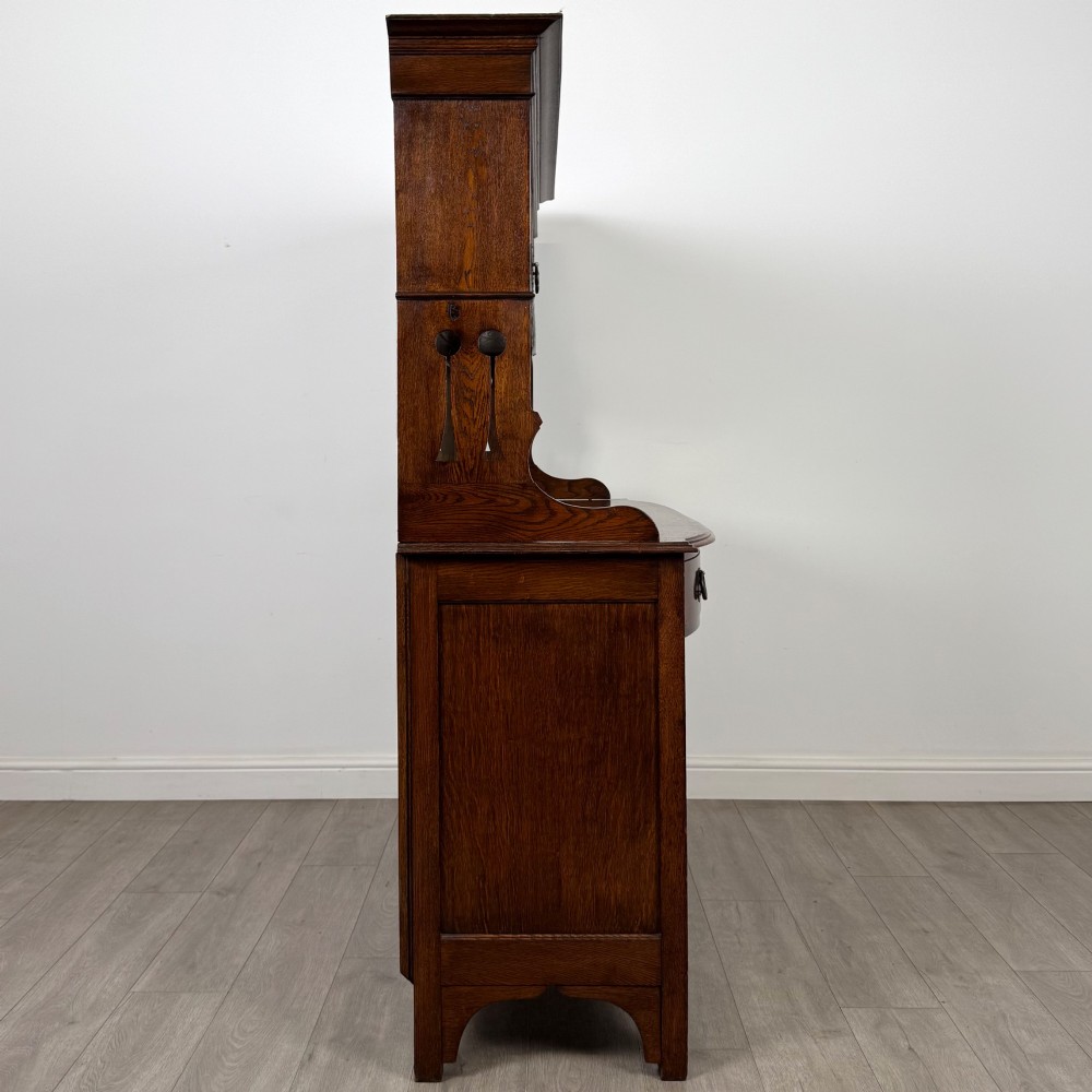 An early twentieth-century Arts and Crafts oak sideboard featuring carved floral door panels, two drawers, a mirrored backsplash, and an upper glazed cabinet. View IX