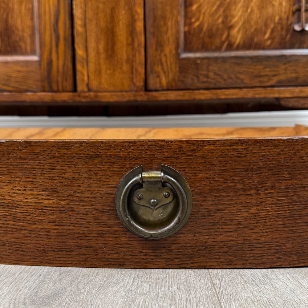 An early twentieth-century Arts and Crafts oak sideboard featuring carved floral door panels, two drawers, a mirrored backsplash, and an upper glazed cabinet. View XIII