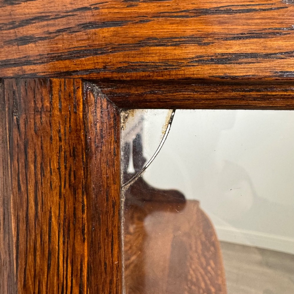 An early twentieth-century Arts and Crafts oak sideboard featuring carved floral door panels, two drawers, a mirrored backsplash, and an upper glazed cabinet. View XIV