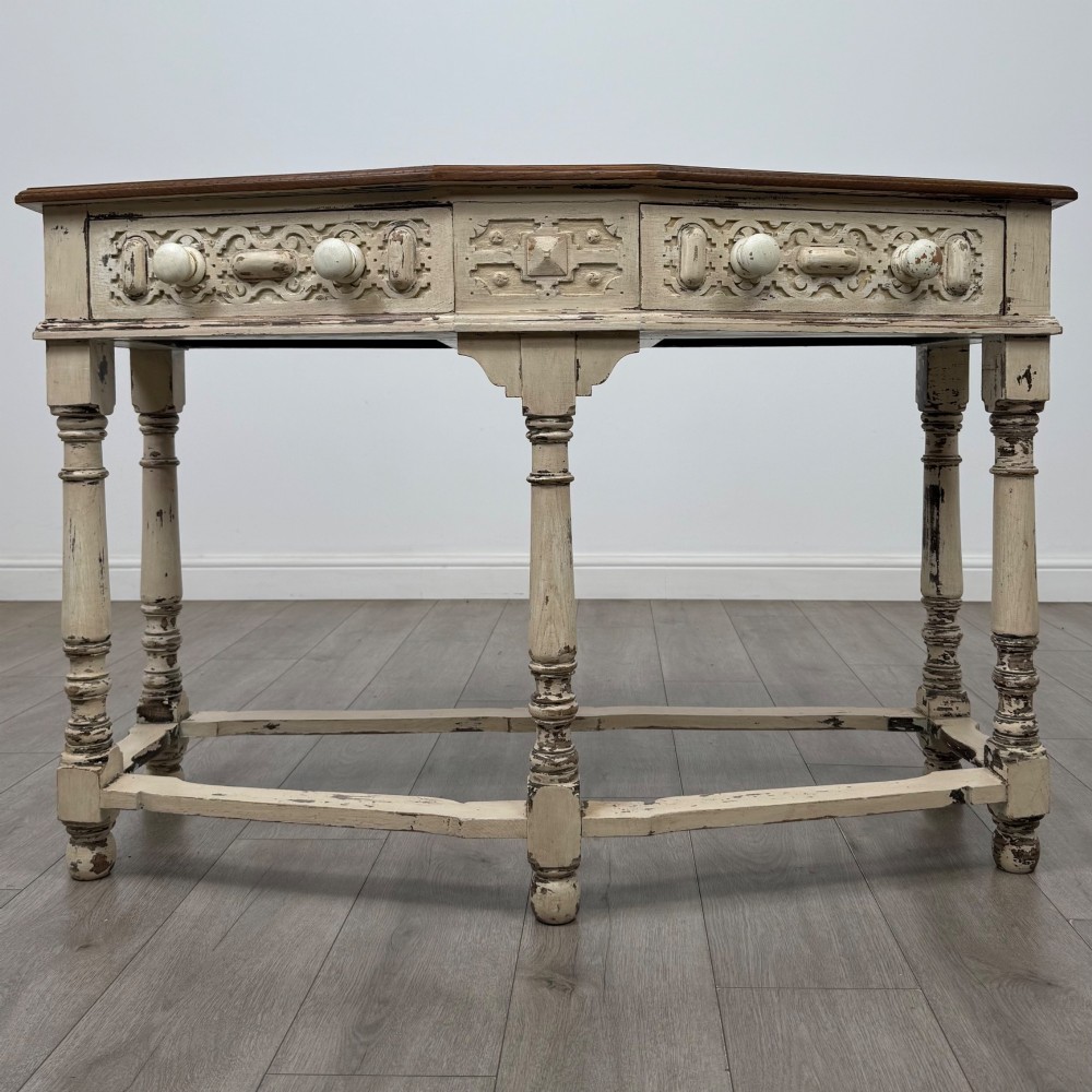 A 20th-century country house style console table featuring a distressed cream-painted carved base with five turned legs and a polished dark oak top.