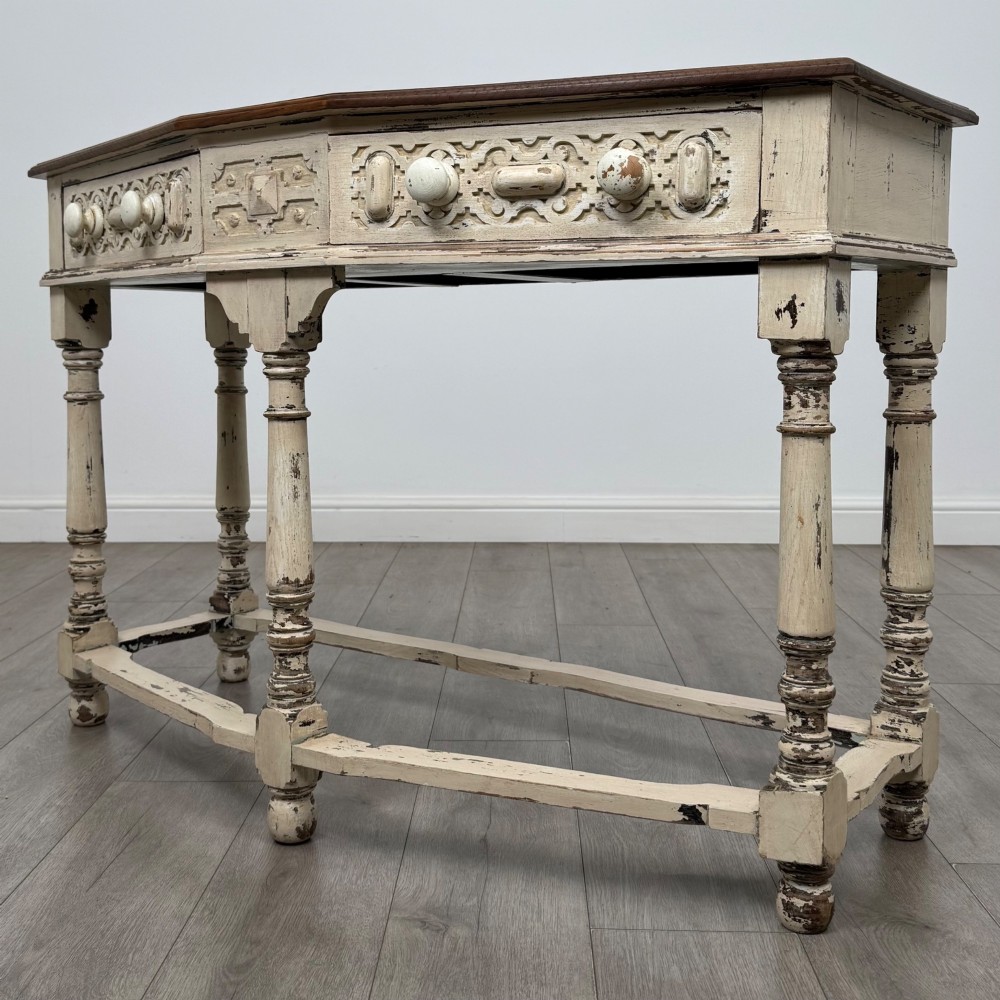 A 20th-century country house style console table featuring a distressed cream-painted carved base with five turned legs and a polished dark oak top. View II
