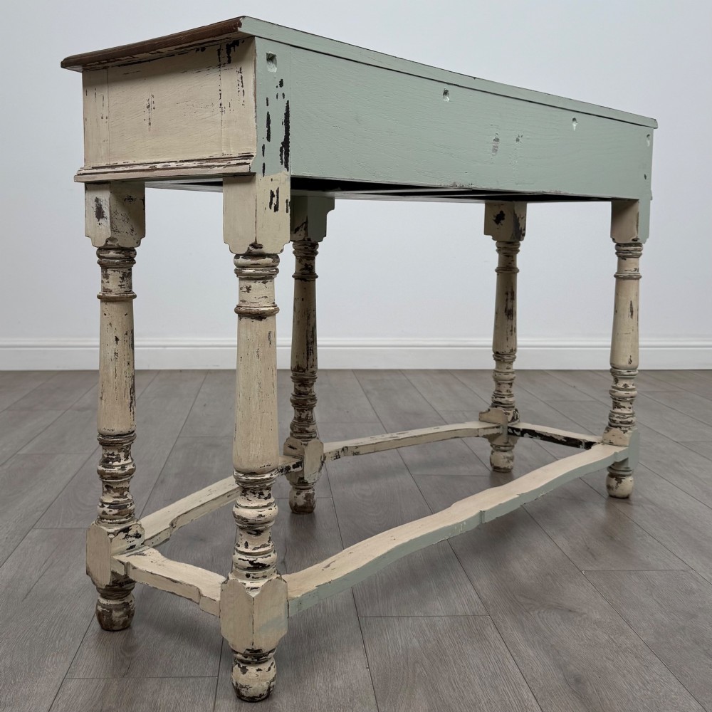 A 20th-century country house style console table featuring a distressed cream-painted carved base with five turned legs and a polished dark oak top. View IV