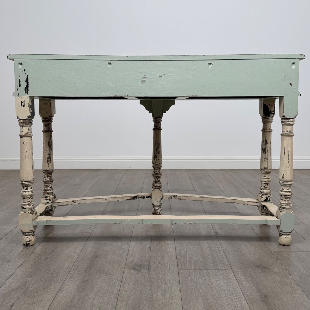 A 20th-century country house style console table featuring a distressed cream-painted carved base with five turned legs and a polished dark oak top. View V