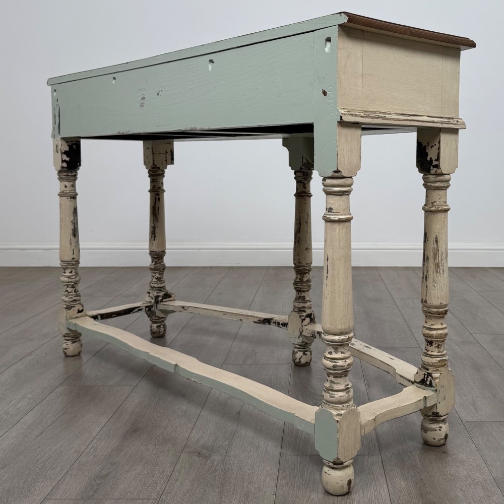 A 20th-century country house style console table featuring a distressed cream-painted carved base with five turned legs and a polished dark oak top. View VI