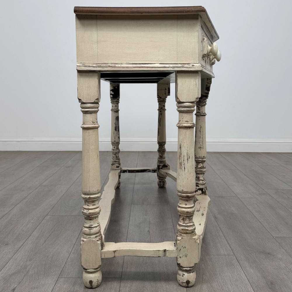 A 20th-century country house style console table featuring a distressed cream-painted carved base with five turned legs and a polished dark oak top. View VII
