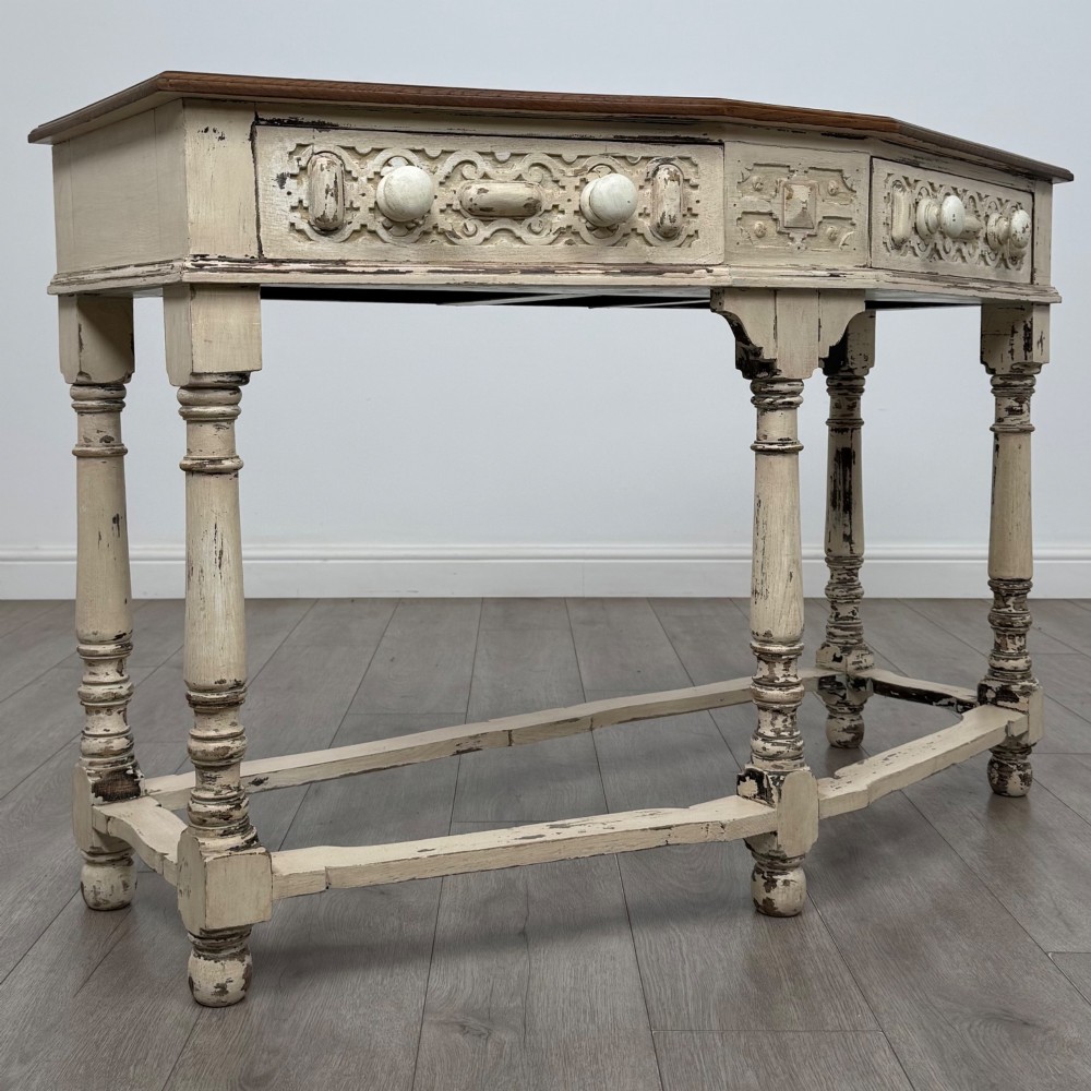 A 20th-century country house style console table featuring a distressed cream-painted carved base with five turned legs and a polished dark oak top. View VIII
