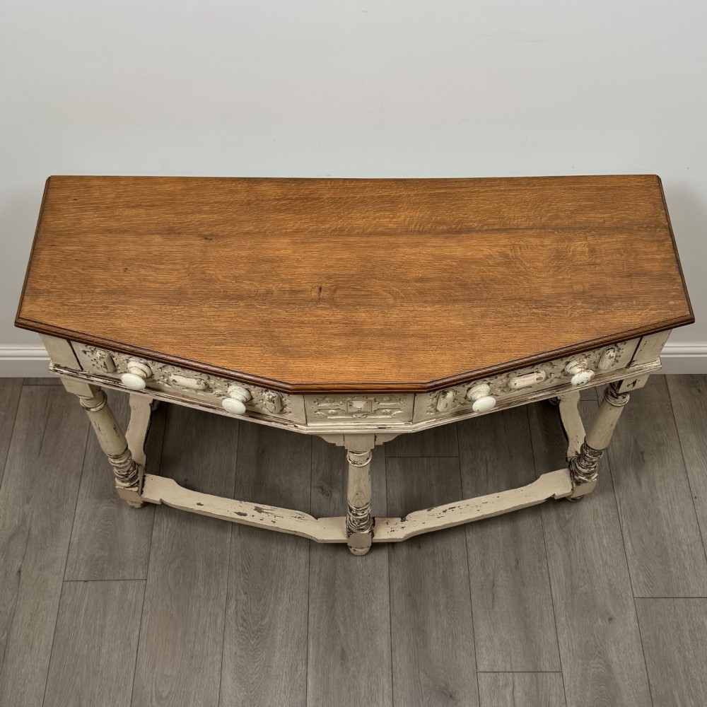 A 20th-century country house style console table featuring a distressed cream-painted carved base with five turned legs and a polished dark oak top. View IX