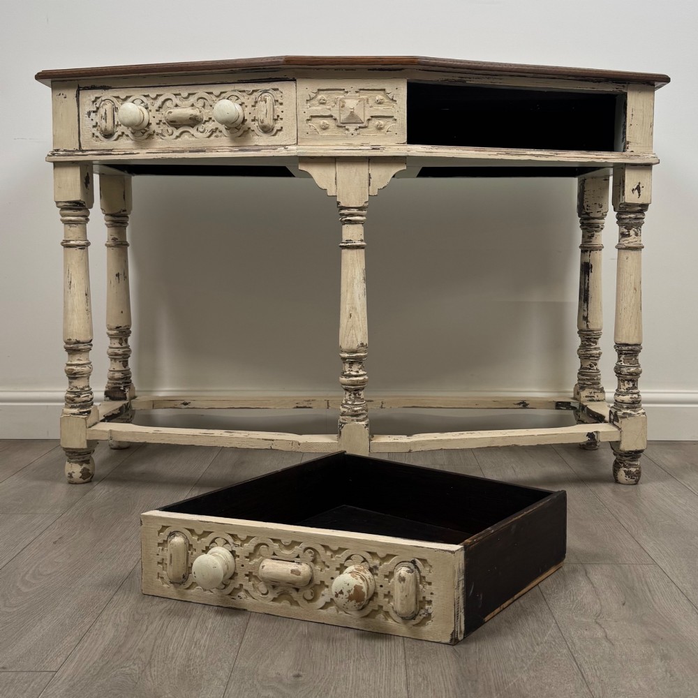A 20th-century country house style console table featuring a distressed cream-painted carved base with five turned legs and a polished dark oak top. View X