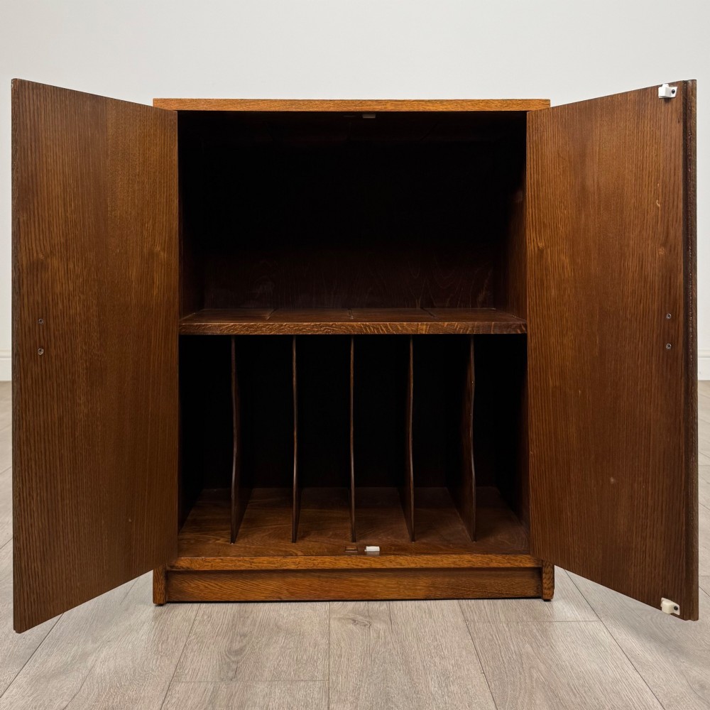 A freestanding golden oak cupboard featuring two flush rectangular doors with matching wooden block handles and brass hinges. View II