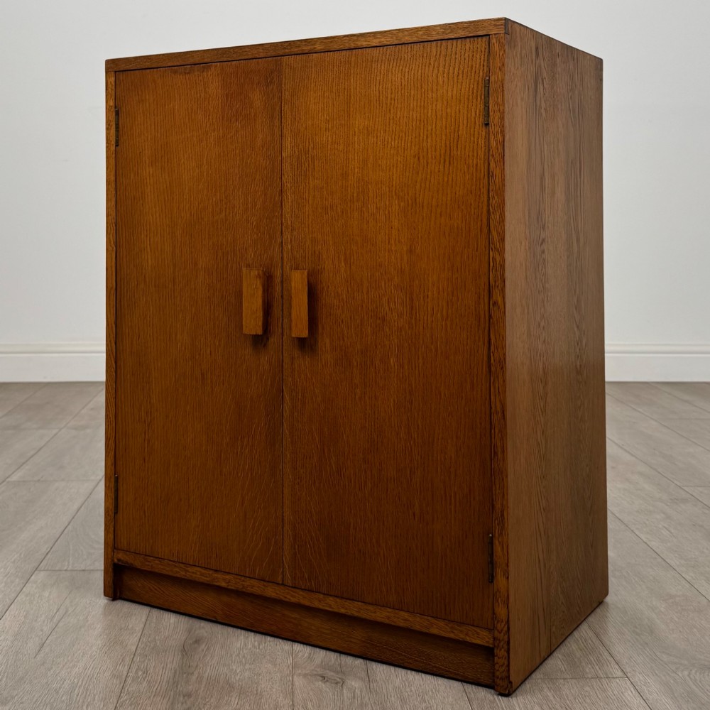 A freestanding golden oak cupboard featuring two flush rectangular doors with matching wooden block handles and brass hinges. View III