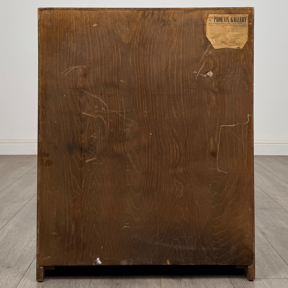 A freestanding golden oak cupboard featuring two flush rectangular doors with matching wooden block handles and brass hinges. View VI