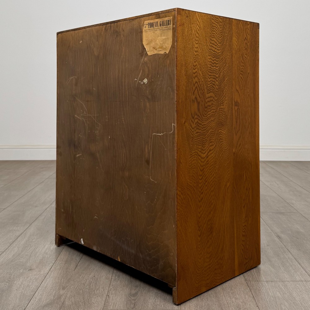 A freestanding golden oak cupboard featuring two flush rectangular doors with matching wooden block handles and brass hinges. View VII