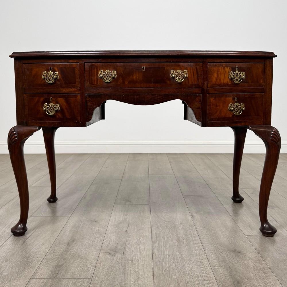 An Edwardian mahogany writing table featuring five drawers with decorative brass handles, a central kneehole apron, and carved cabriole legs.