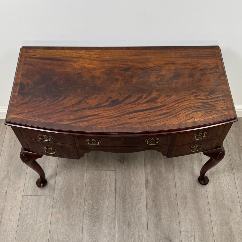 An Edwardian mahogany writing table featuring five drawers with decorative brass handles, a central kneehole apron, and carved cabriole legs. View IX