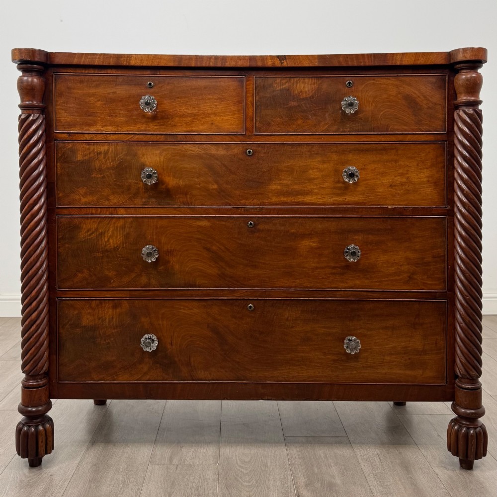 A 19th-century Regency mahogany chest of drawers featuring two short over three long graduated drawers, decorative spiral-twist side columns, glass knobs, and turned carved feet.