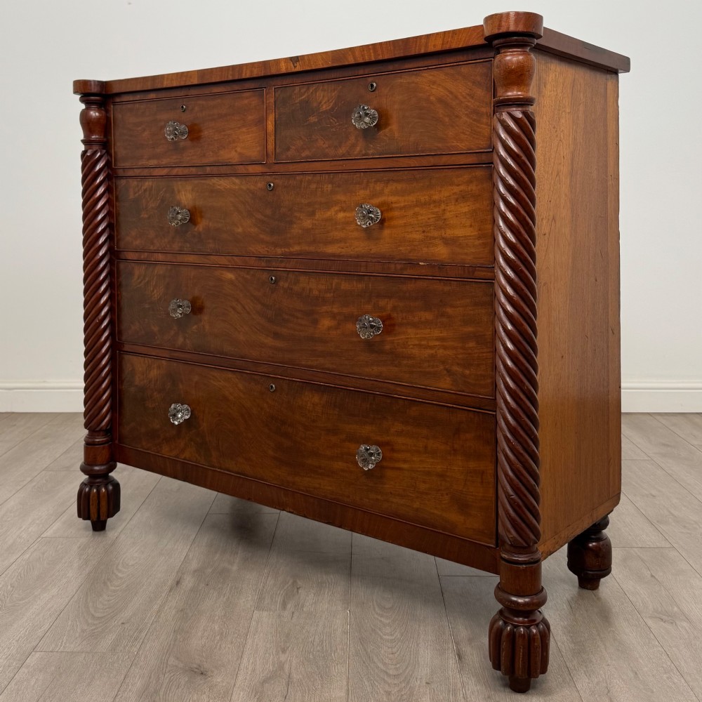 A 19th-century Regency mahogany chest of drawers featuring two short over three long graduated drawers, decorative spiral-twist side columns, glass knobs, and turned carved feet. View II