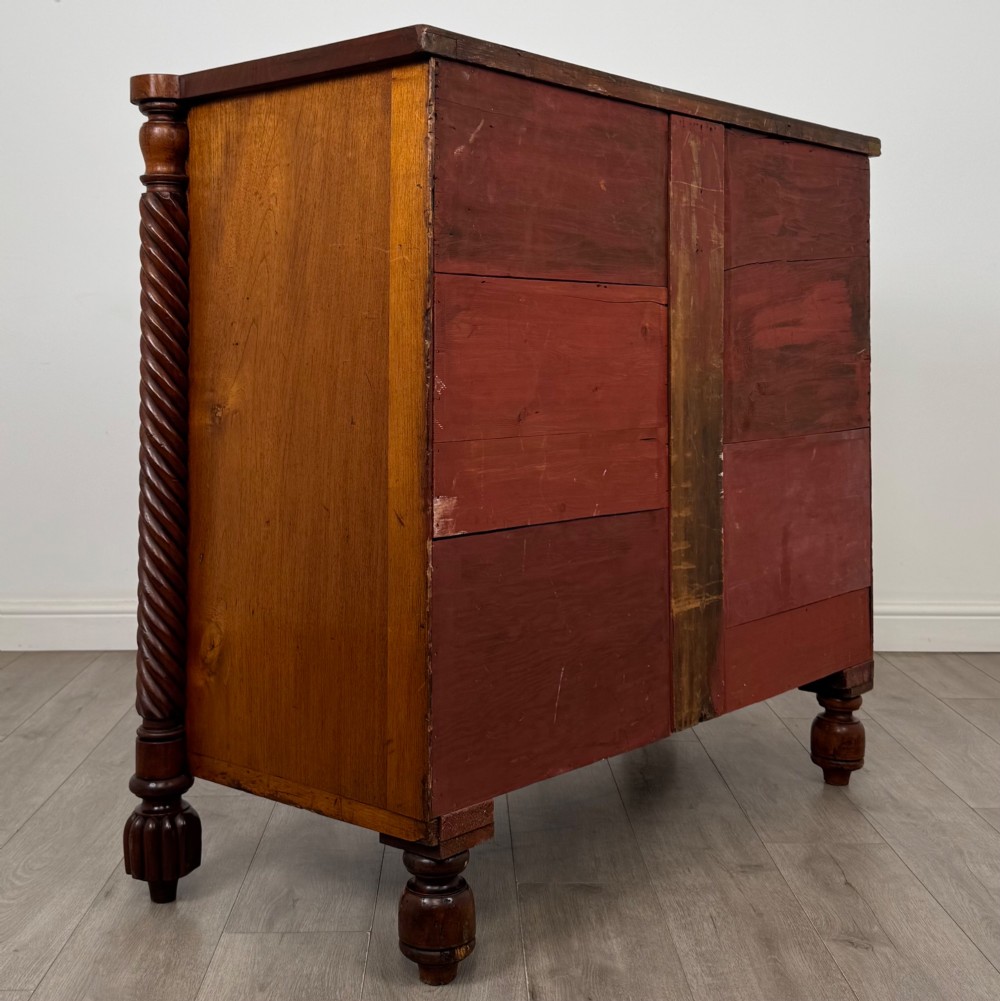 A 19th-century Regency mahogany chest of drawers featuring two short over three long graduated drawers, decorative spiral-twist side columns, glass knobs, and turned carved feet. View IV