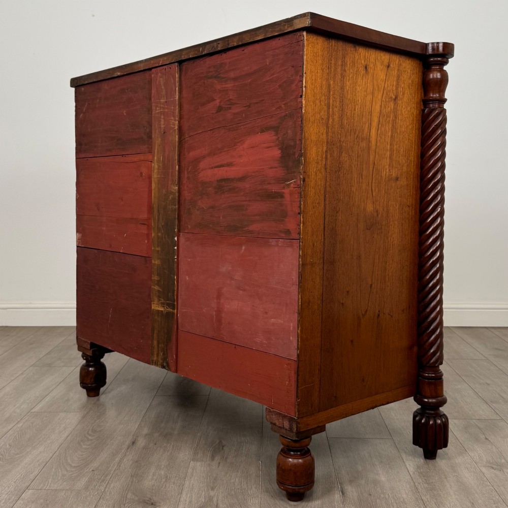 A 19th-century Regency mahogany chest of drawers featuring two short over three long graduated drawers, decorative spiral-twist side columns, glass knobs, and turned carved feet. View VI