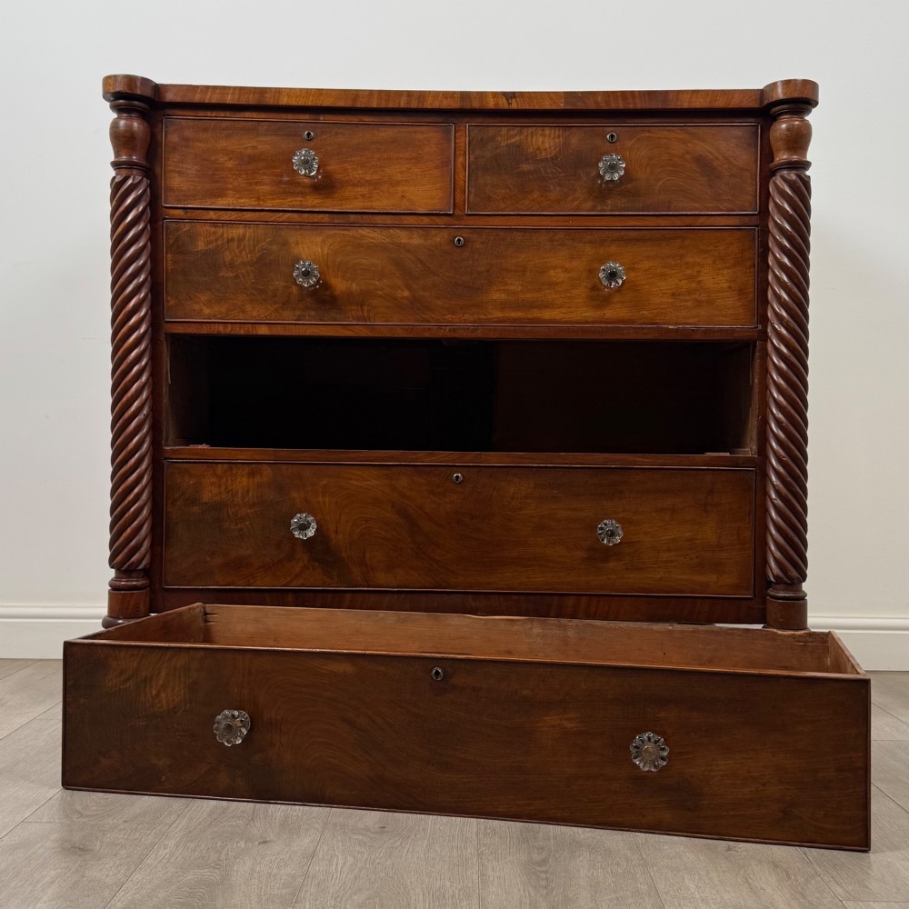 A 19th-century Regency mahogany chest of drawers featuring two short over three long graduated drawers, decorative spiral-twist side columns, glass knobs, and turned carved feet. View X