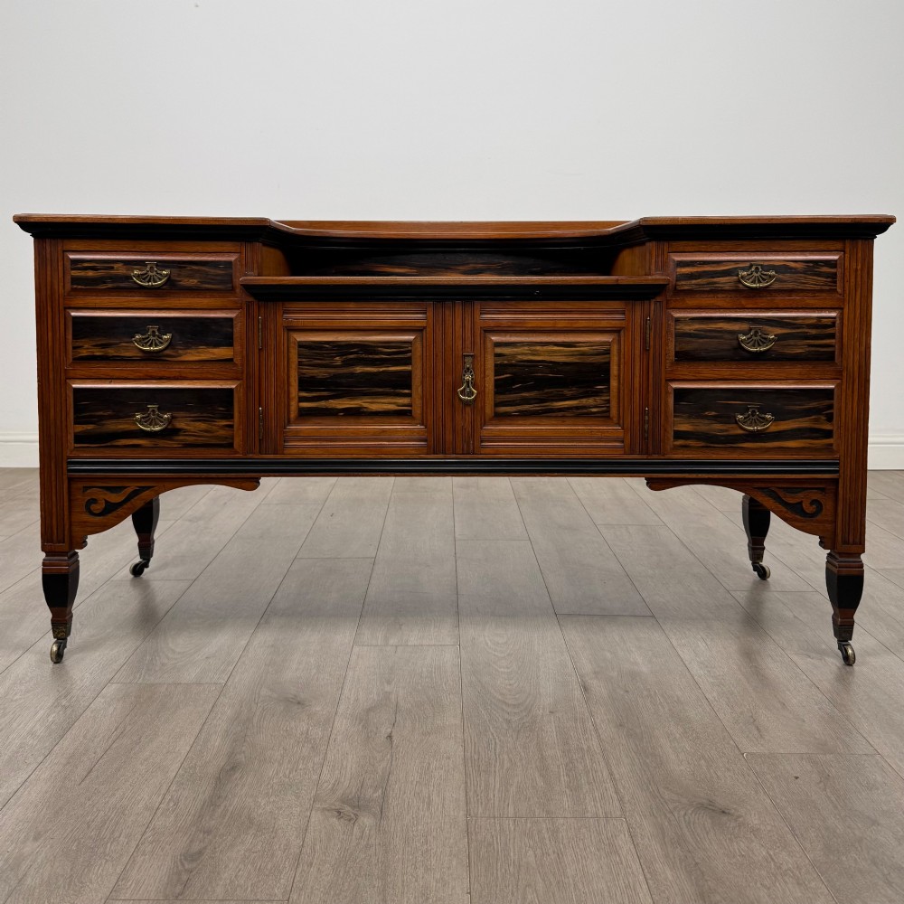 An antique mahogany low sideboard featuring six drawers, a central double cupboard, highly figured veneer panels, brass handles, and turned legs on castors.