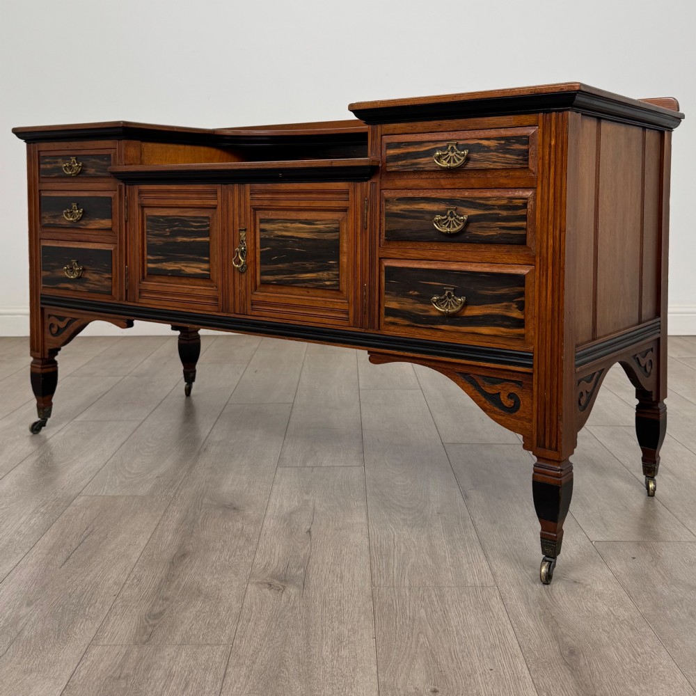 An antique mahogany low sideboard featuring six drawers, a central double cupboard, highly figured veneer panels, brass handles, and turned legs on castors. View III